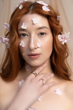 Mutlu genç bir kadın şık bir kıyafetle parlak bir stüdyoda çiçeklerle poz veriyor..