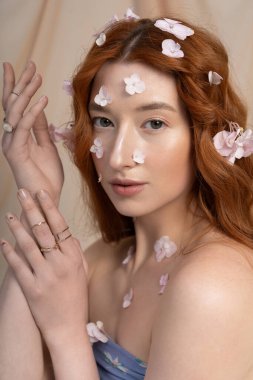 Genç kızıl saçlı bir kadın zarif bir şekilde çiçeklerle poz veriyor. Stüdyoda baharın güzelliğini temsil ediyor..