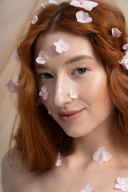 Bahar modasında neşeli genç bir kadın zarif çiçeklerle çevrili bir stüdyoda poz veriyor..