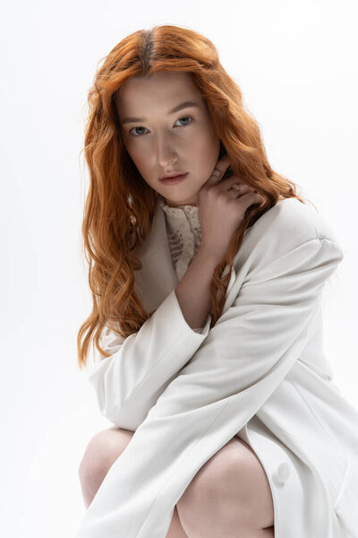 A young woman with striking red hair poses gracefully in a sleek studio, embodying spring style.