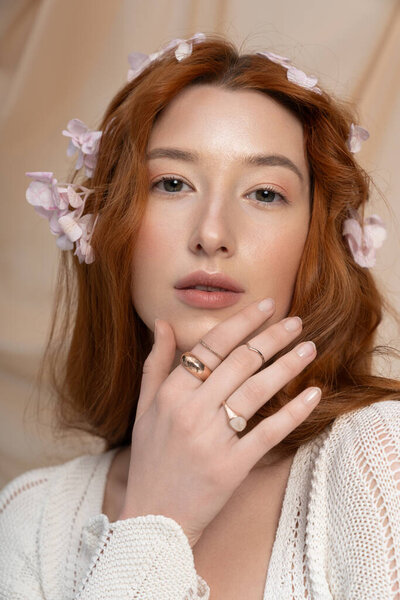 A young redhead poses gracefully with flowers, embodying the essence of spring fashion in a studio.