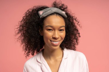 Genç bir kadın, modaya uygun bir uyku elbisesi ve kedinin saç bandıyla neşeli bir şekilde gülümsüyor..