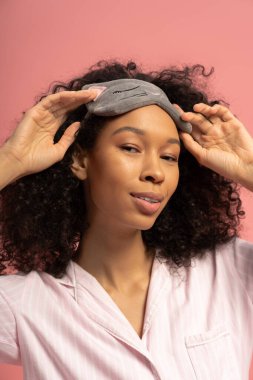 Güzel, genç bir kadın şık uyku maskesini, ışık saçan cazibesini ve kendine güvenini şakayla ayarlıyor..