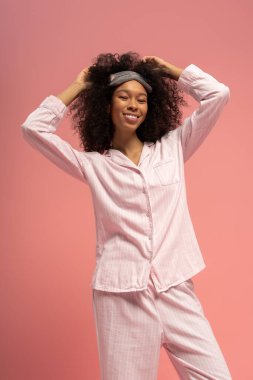 Genç bir kadın pembe bir arka planda şık pijamalarıyla neşeli pozlar veriyor..