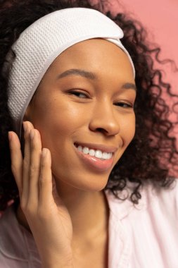 Neşeli bir yüzü olan zarif genç bir kadın eğlenceli bir an için poz verirken nazikçe yüzüne dokunur..