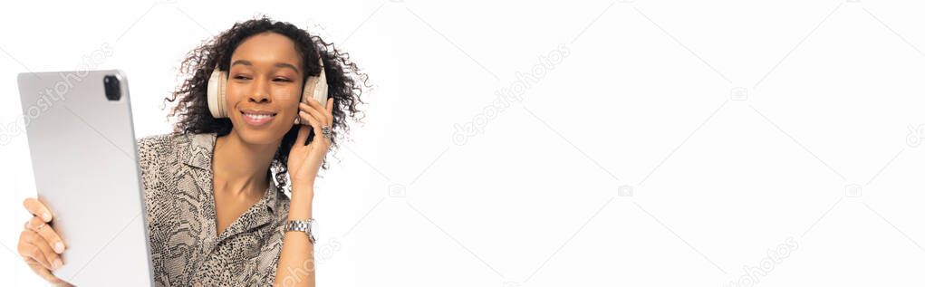 Яркая и веселая молодая женщина слушает музыку на планшете, в модных наушниках.