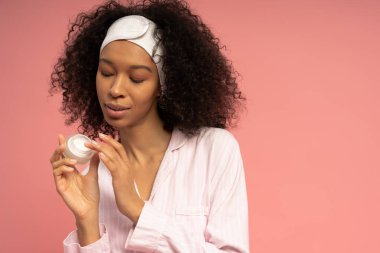 Neşeli genç bir kadın krem sürüyor, derisine işlemiş pembe bir zemine.