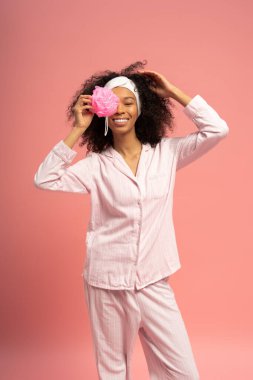 Zarif genç bir kadın, yumuşak pembe pijamaları ve saçında çiçekle ışıl ışıl gülümser..