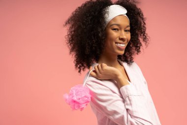 Tarz sahibi genç bir kadın, pembe bir arka plana karşı neşeyle renkli bir banyo aksesuarı tutuyor..