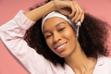 Güzel genç bir kadın cilt bakımını sever. Gülümserken zarafetle serumu uygular..