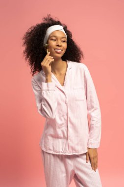 Cilt bakımı yaparken gülümseyen, neşeli bir arka planda şık pijamalar giyen genç bir kadın..