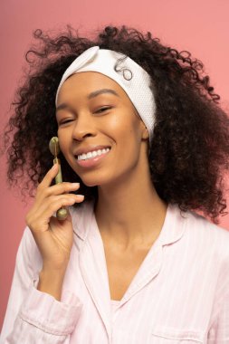 Güzel genç bir kadın mutlu bir şekilde yüzüne yeşim bir silindir takıyor pembe bir zemine karşı.