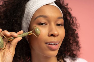 Şık bir genç kadın, bir anlık özgüvenini kucaklarken parıldayan yüzünde yeşim bir silindir kullanır..