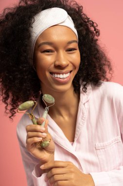 Genç bir kadın yeşim taşları canlı pembe bir zemin üzerinde tutarken kendine güven yayıyor..