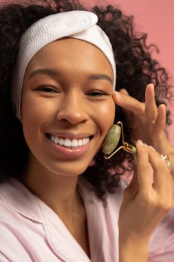 Gülümseyen genç kadın, parlayan cilt için yeşim bir silindir kullanarak güzellik rutinini geliştirir..