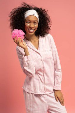 Neşeli bir kadın pembe bir banyo lifini tutar, parlak bir arka plana karşı şık uykusunu sergiler..