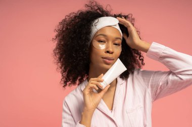 Şık, genç bir kadın, pembe bir arka plana cilt kremi sürüyor..