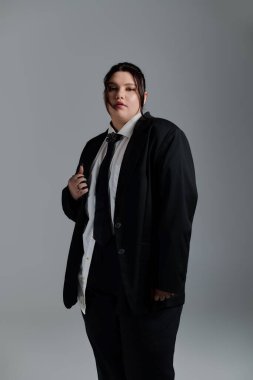 Kendine güveni tam ve iri bir kadın modern modaya uygun siyah bir takım elbise ve çarpıcı bir pozla bürünür..