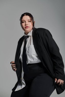 Kendine güveni tam ve cüsseli bir kadın terzi kıyafeti giymiş, çağdaş moda eğilimlerini somutlaştırıyor..