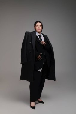 Siyah takım elbiseli şık bir kadın gri bir arka plana karşı güven yayıyor..