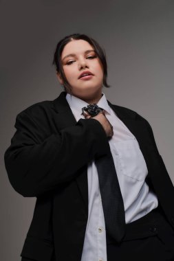 Kendine güveni tam ve cüsseli bir kadın, özel dikim siyah bir takım elbise içinde, cesur bir poz veriyor..