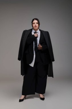 Güzel, iri yarı bir kadın şık bir kıyafet içinde duruyor, kendine güveni ve zarafeti var..