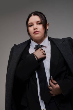 Çekici, iri yarı bir kadın şık siyah takım elbise ve kravatıyla eşsiz tarzını sergiliyor..