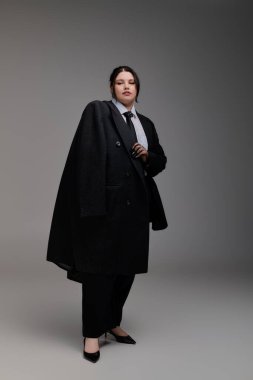 Siyah cüsseli, güzel ve cüsseli bir kadın minimalist bir yerde duruyor..