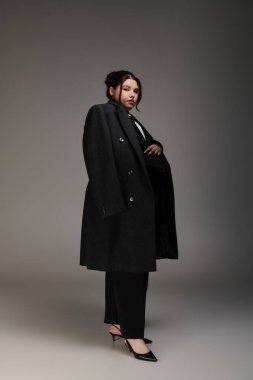 Güzel ve iri yarı bir kadın şık siyah bir ceket içinde kendine güvenerek poz verir. Zarafet ve cazibe saçar..