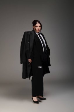 Göz kamaştırıcı, iri yarı bir kadın, modern zarafeti yansıtan şık siyah bir takım elbise giyer..