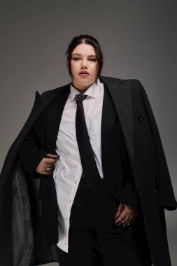 Şık ve cüsseli bir kadın özel dikim bir takım elbise ve ceket içinde zarafet sergiliyor. Kendine güveni ve tarzı var..