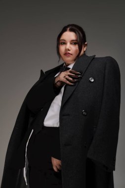 Ayrıca cüsseli bir kadın büyük bir ceket ve özel dikim kıyafetle modern zarafet sergiliyor..