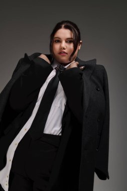 Güzel, iri yarı bir kadın şık siyah bir ceket ve kravatla göz kamaştırıcı bir şekilde poz verir..