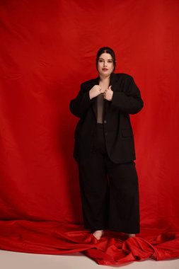 Kendine güveni tam ve cüsseli bir kadın şık siyah bir elbise içinde cesurca duruyor..