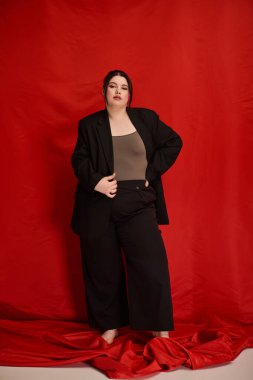 Kendine güvenen bir kadın, çarpıcı kırmızı bir arka planla modern modayı şık bir şekilde sergiliyor.