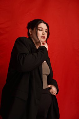 Tarz sahibi, iri yarı bir kadın gururla poz verir canlı kırmızı bir arka plana, göz alıcı bir çekiciliğe.