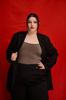 Kendine güveni tam ve cüsseli bir kadın kırmızı bir arkaplanda şık bir şekilde poz veriyor..