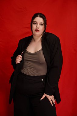 Kendine güvenen ve cüsseli bir kadın şık bir elbiseyle koyu kırmızıya karşı gösteriş yapar..