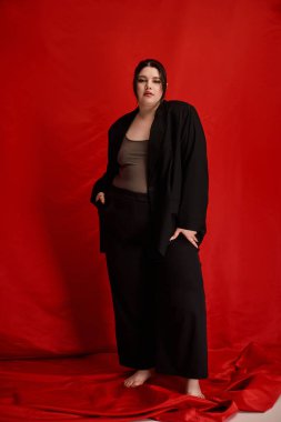 Cesur ve cüsseli kadın, parlak kırmızı bir arka plana karşı zarif bir şekilde duruyor, kendine güveni ve stili yayıyor..