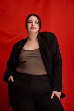 Kendine güvenen ve cüsseli bir kadın modeller koyu kırmızı bir arka plana karşı şık giyinirler..