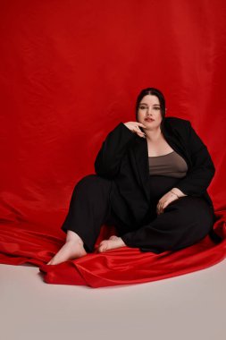 Güzel, iri yarı bir kadın zarif poz verir, şık elbisesini ve kendine güvenen tavırlarını sergiler..