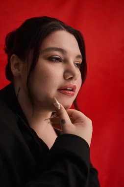 Çekici ve cüsseli kadın, canlı kırmızı bir fon karşısında güzelliğini ve modasını ön plana çıkarıyor..