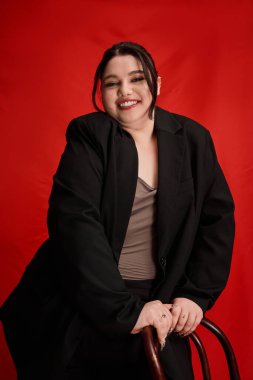 Güzel, iri yarı bir kadın, bir sandalyeyle neşe içinde poz verirken moda anlayışını sergiliyor..