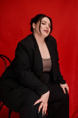 Şık ve iri yarı bir kadın zarif bir şekilde otururken şık bir siyah takım elbiseye güvenir..