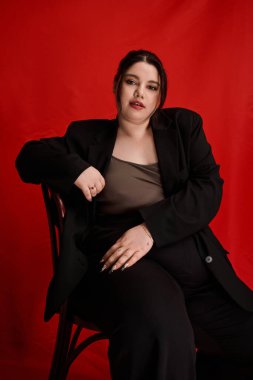 Şık giyinmiş kendine güvenen ve güzel bir kadın zarif bir şekilde kırmızı arka plana karşı duruyor..