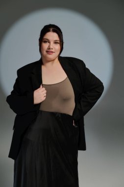 Güzel ve iri yarı bir kadın, tarafsız bir arkaplana karşı şık bir elbiseyle rahatça poz veriyor..