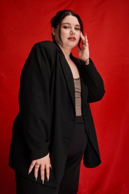 Çarpıcı ve cüsseli bir kadın, özel dikim bir elbise içinde çarpıcı bir arka plana karşı zarafet yayar..