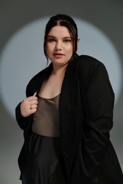 Güzel, iri yarı bir kadın şık bir siyah ceketle moda anlayışını sergileyerek kendine güvenerek poz veriyor..