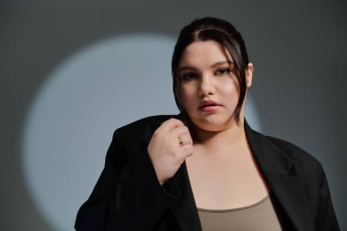 Güzel ve iri bir kadın, benzersiz tarzını yumuşak ışıklandırma altında şık bir pozda sergiliyor..