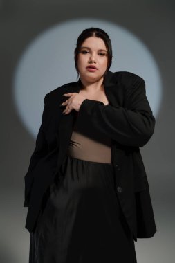 Ayrıca cüsseli bir kadın modern bir kıyafetle özgüven ve zarafet yayar, düşünceli bir poz verir..